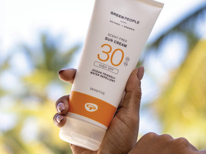A hand holding a Green People sun cream product