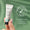 A hand holds a small white tube of Rejuvenating Eye Cream 10ml against a sage green background with leaf shadows.