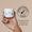 Una mano sostiene una jarra blanca de Organic Babies Soothing Baby Salve junto a un logo "Dermatológicamente Testado" sobre un fondo beige.