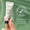 Mano sostiene un tubo de crema para ojos sin perfume Green People 10ml sobre fondo verde con icono de "dermatológicamente probado".