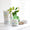 Un tarro blanco de bálsamo reparador para mamá y bebé Organic Babies sobre una superficie brillante junto a un ratón de juguete de madera y un florero verde.
