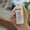 Hand holding a white pump bottle of moisturizer with silver trim, angled left with blurred green and brown background.