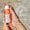 Hände halten eine orange-weiße Flasche Oy Clear Skin Reinigungscreme mit dem Abzeichen „Dermatologisch getestet“.